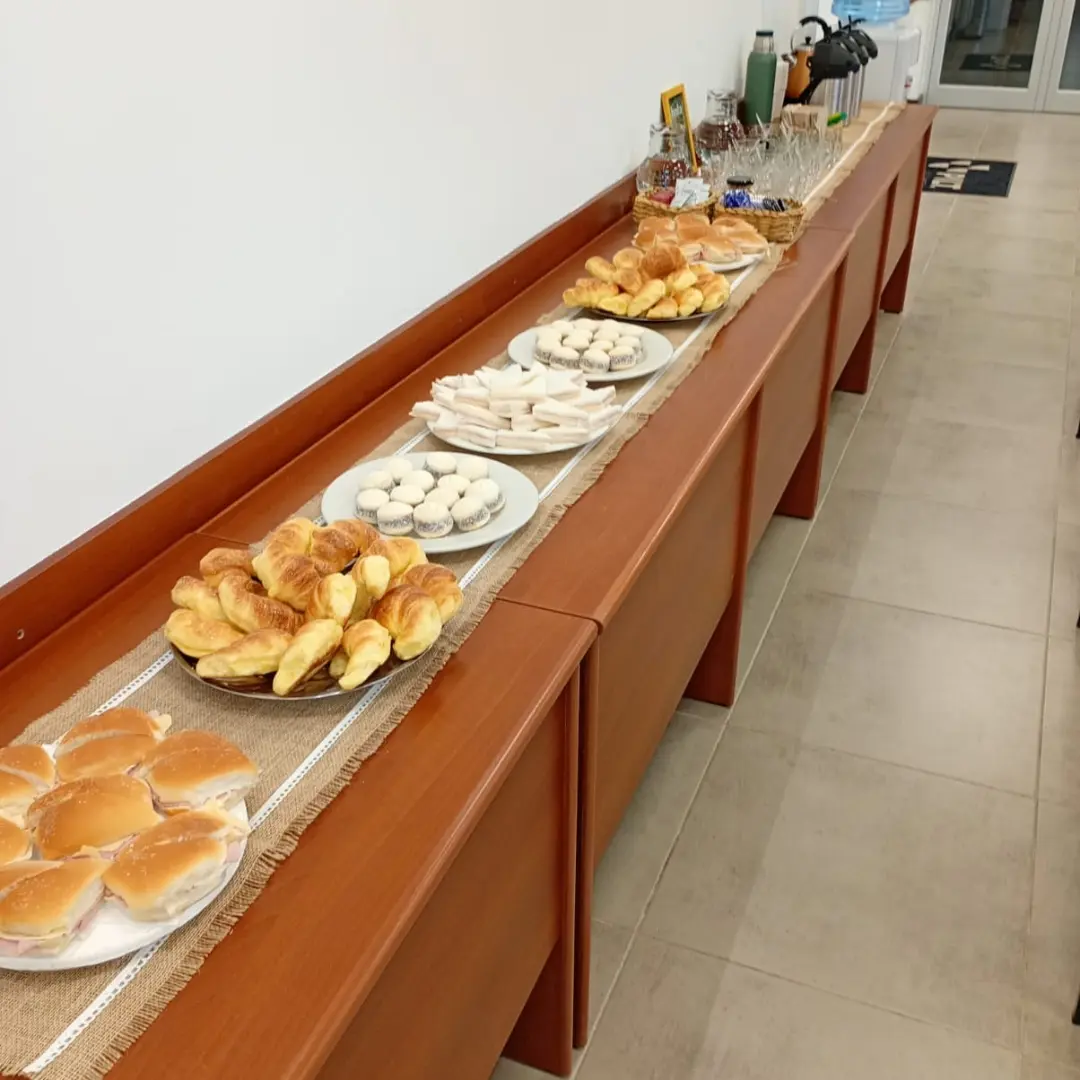 Mesa larga de coffee break corporativo de Enjoy y a picar con sándwiches, medialunas, alfajores de maicena e infusiones calientes.